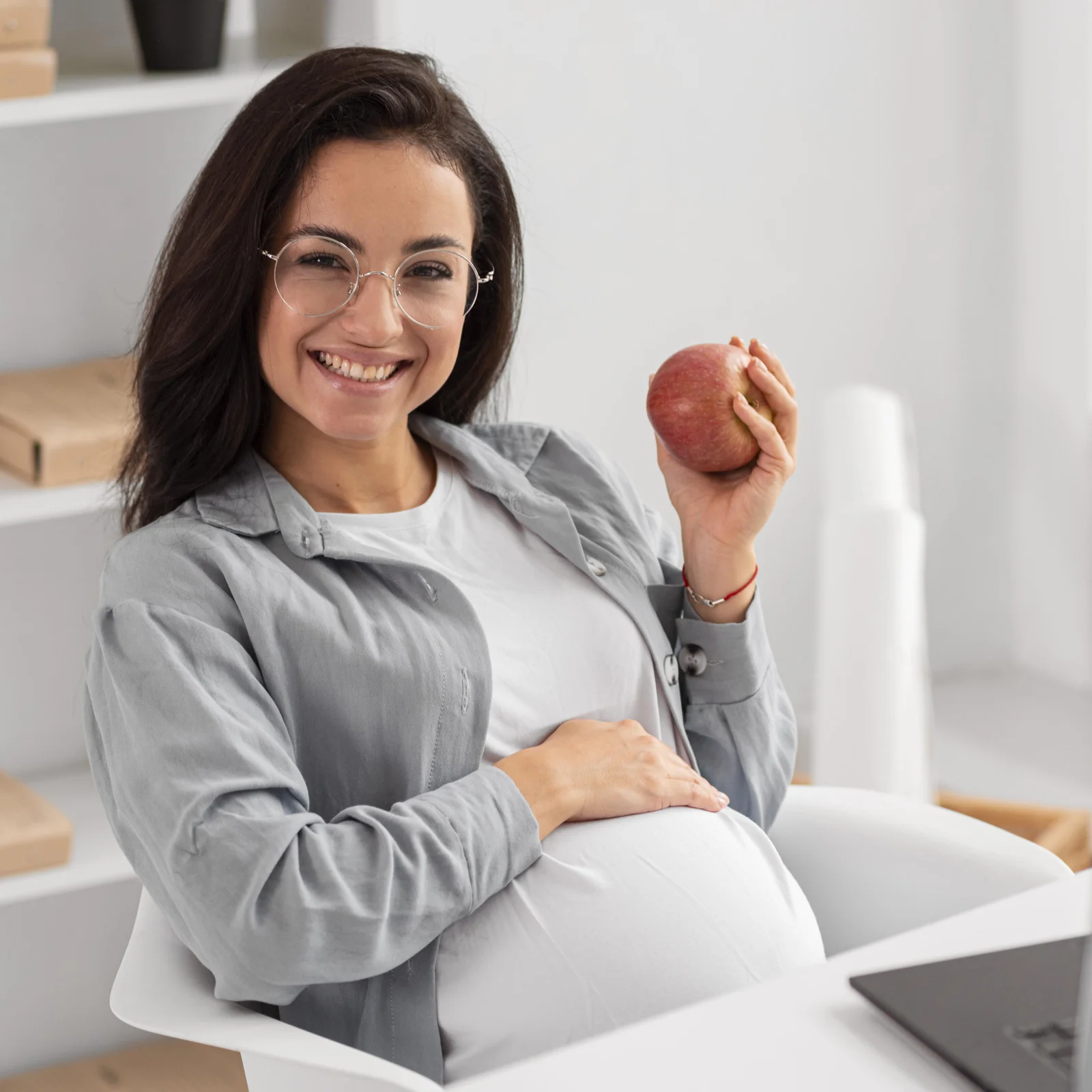 A smiling pregnant woman holding an apple