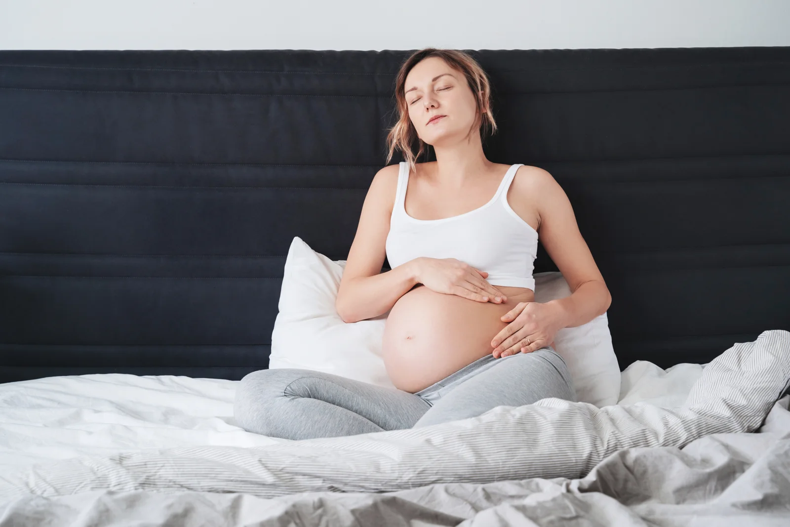 A pregnant woman resting on a bed with one hand on her back