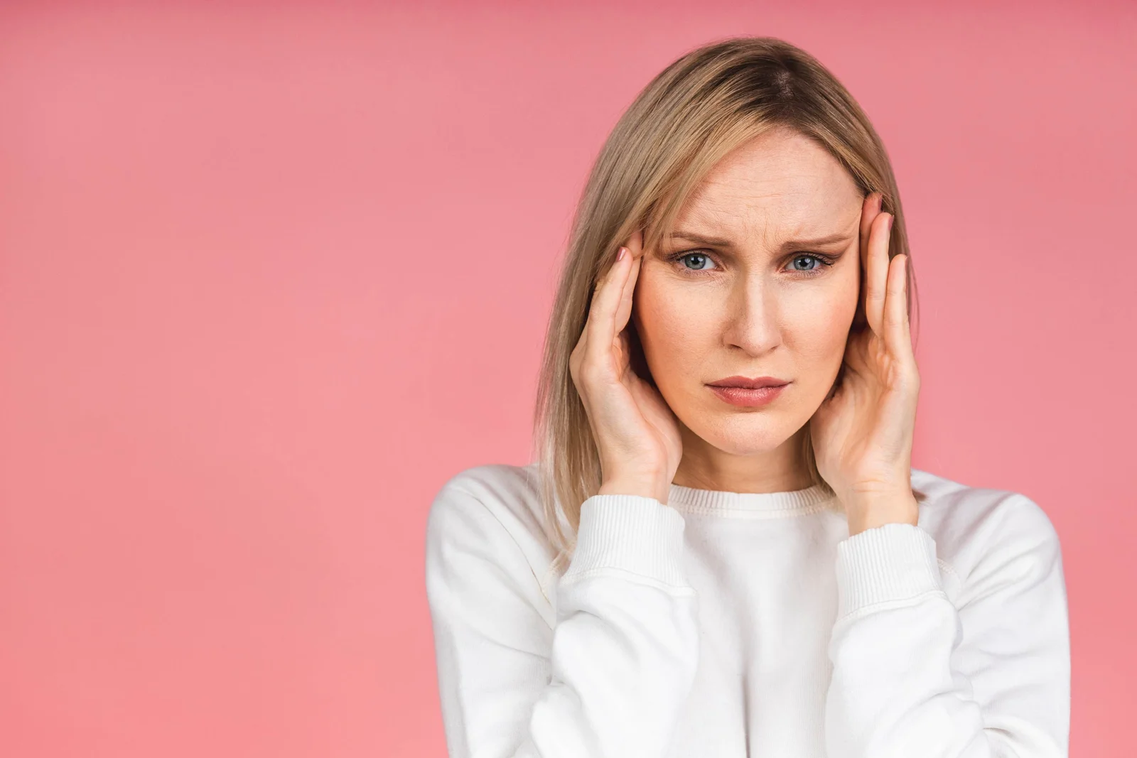 A woman resting her hands on her face against a pink background